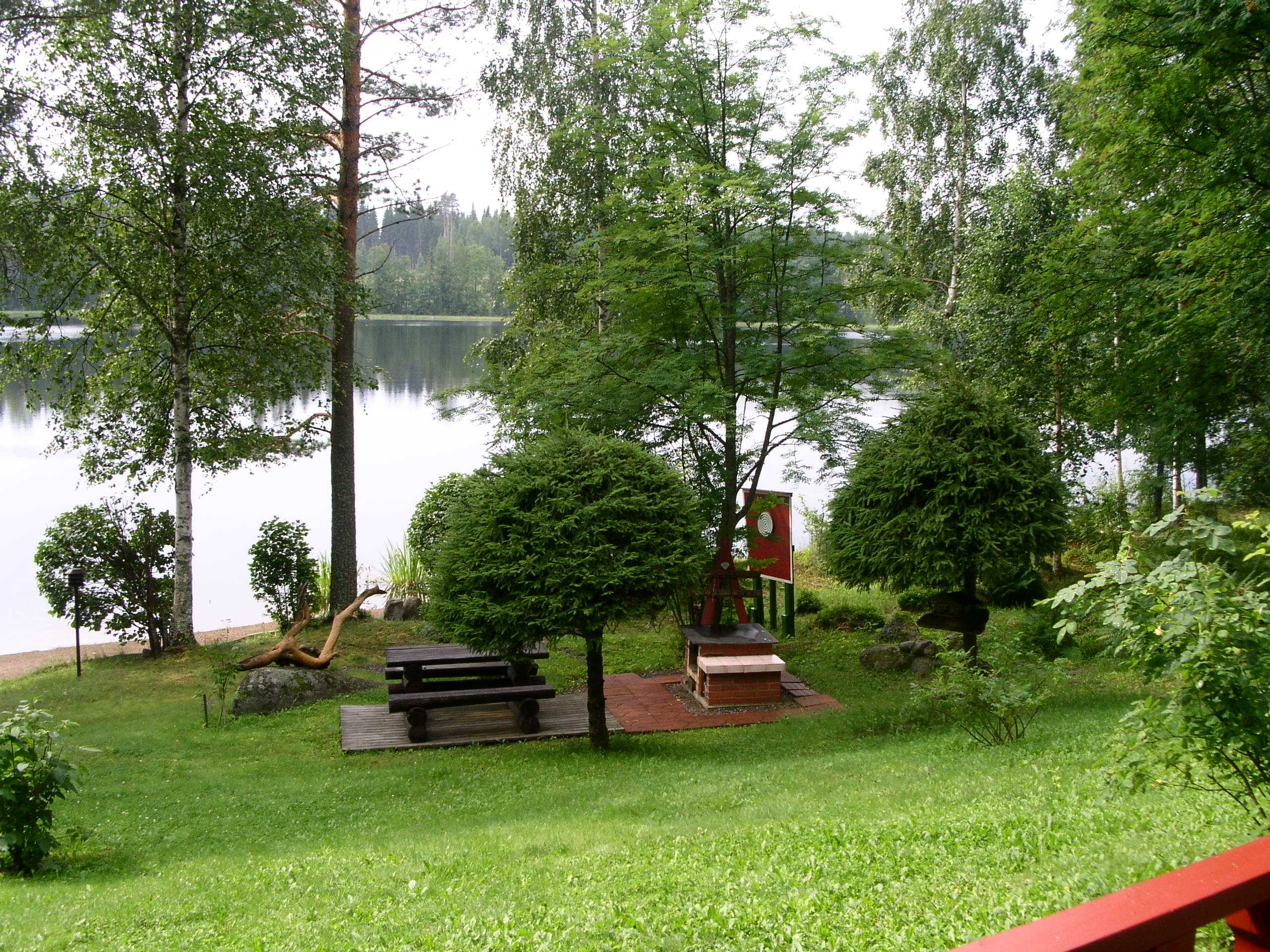 Lakeside garden with mown lawn, picnic table, small barbecue, ornamental trees and shrubs, calm water and forest in back
